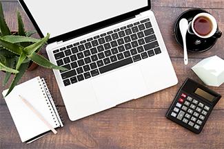 桌子上有一个打开的笔记本电脑，笔记本，计算器，咖啡和尖的龙舌兰植物.